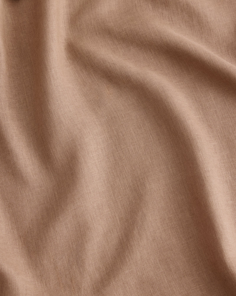 A close-up of draped fabric in a warm taupe-beige colour called Portobello, in 100% French flax linen showing soft folds and a fine woven texture.