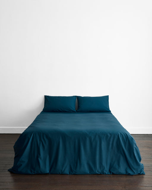 Close-up of the Bed Threads Aegean Organic Cotton in dark teal, showing visible folds and creases that create subtle shadows and texture on the percale surface.