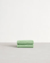 A set of two Apple 100% Cotton Terry Face Washers by Bed Threads, crafted from absorbent, skin-friendly cotton, is neatly folded on a light gray surface with a plain white wall in the background. - view