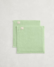 The Bed Threads Apple 100% Cotton Terry Face Washers (Set of Two) are neatly folded, rectangular, light green with small beige labels, crafted from absorbent terry that's gentle on skin and placed on a light textured surface. - view