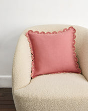 A cream armchair sits against a white wall and wooden floor, topped with Bed Threads' Pink Clay & Terracotta 100% French Flax Linen Arch Cushion Cover featuring scalloped edges, decorative trim, and a zip closure. - view