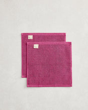 The Berry 100% Cotton Terry Face Washers (Set of Two) by Bed Threads feature soft, absorbent magenta towels with stitched edges and white tags, stacked on a light textured surface—ideal for durable daily face cleansing. - view