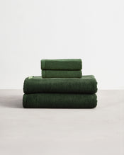 Set of two moss green face washers and two hand towels in 100% cotton terry stacked on a light grey surface with a white background.  - view