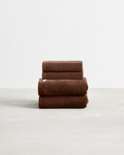 A stack of two, organic cotton terry hand towels and two face washers in an espresso brown shade. - view