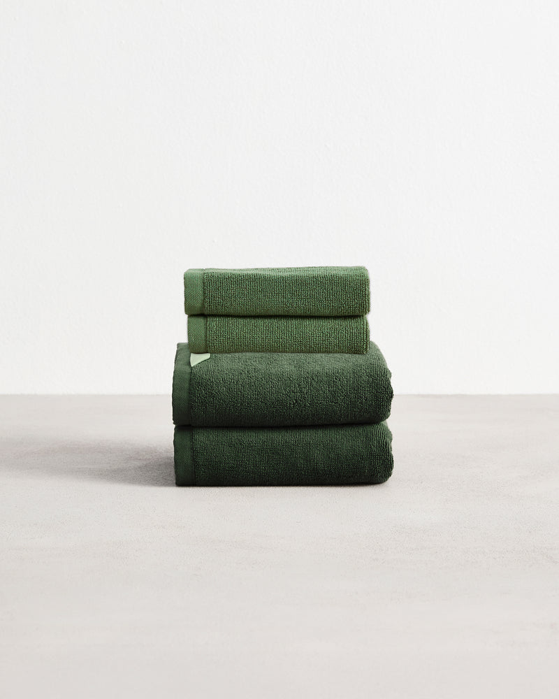 A stack of two, organic cotton terry hand towels and two face washers in a moss green shade.
