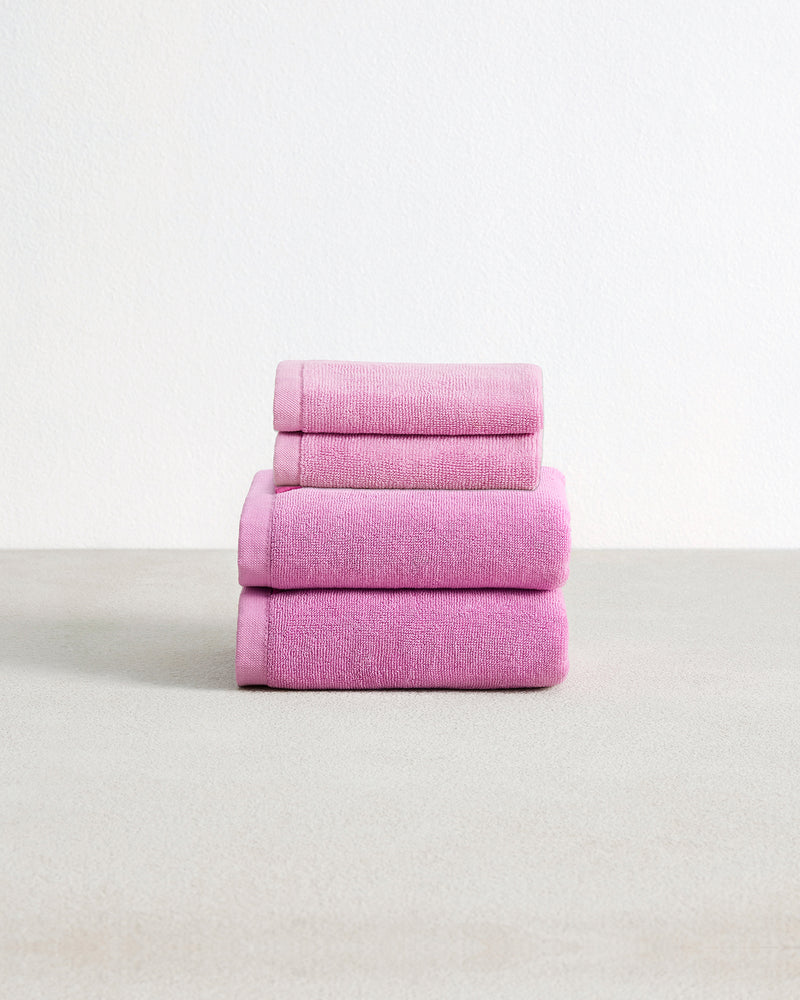 Set of two bubblegum pink face washers and two hand towels in 100% cotton terry stacked on a light grey surface with a white background. 