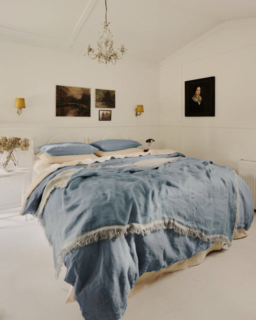 Bedroom with blue and cream bedding with a chandelier and moody artworks on the walls.