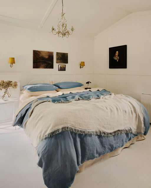 Bedroom with a bed covered in blue and cream bedding, framed pictures on the wall, and a chandelier.
