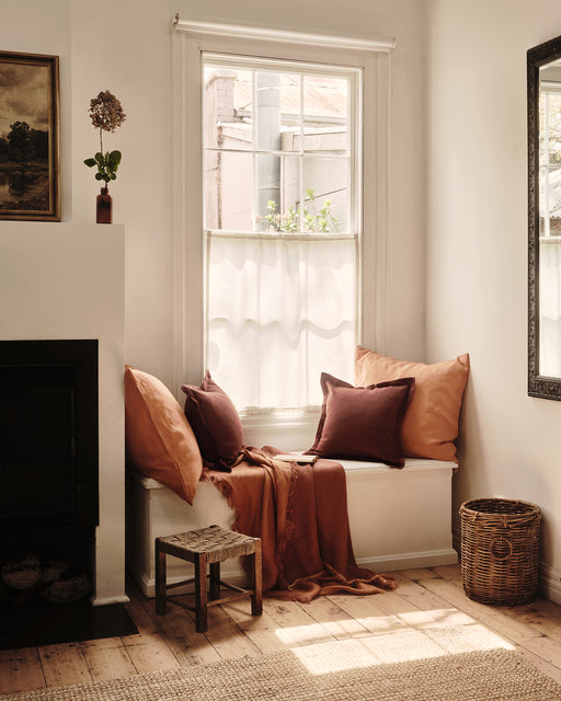 Nook with pillows, a blanket, and cushions by a window in a cozy room.