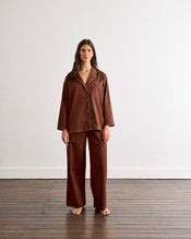 A woman stands barefoot on a wooden floor in front of a plain white wall, wearing the Bed Threads Espresso & Sky Piped Long Sleep Set. - view