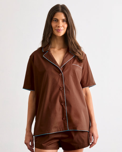 A woman with long brown hair wears the Bed Threads Espresso & Sky Piped Short Sleeve Shirt and matching shorts—lightweight cotton sleepwear—against a plain light background, ideal for warm nights.