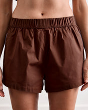 A person wearing the Bed Threads Espresso & Sky Piped Short Sleep Set, featuring brown piped shorts with an elastic waistband and a short sleeve shirt, shown from waist to mid-thigh against a neutral background. - view