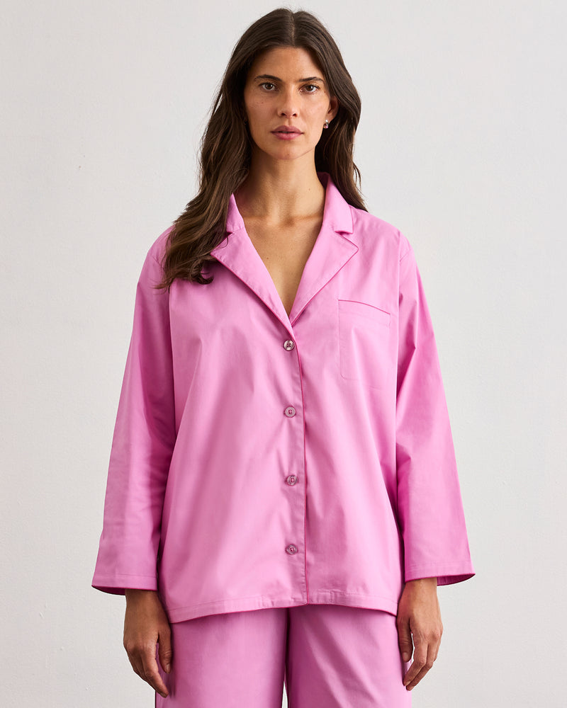 A woman with long brown hair faces forward in a loose-fitting Bubblegum & Berry Piped Long Sleeve Shirt by Bed Threads, featuring soft cotton and contrast piping, set against a plain light background.