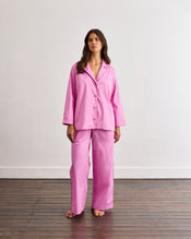 A woman stands barefoot on a wooden floor, wearing the Bed Threads Bubblegum & Berry Piped Long Sleeve Shirt, crafted from soft cotton with subtle contrast piping, against a plain white wall. - view
