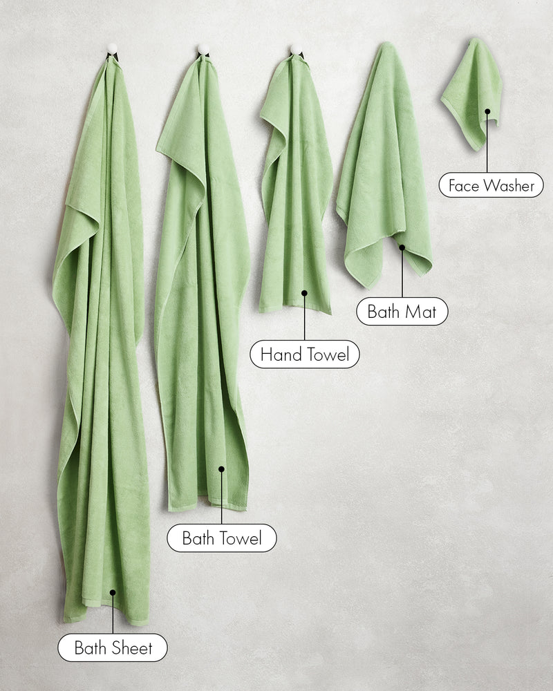 Five light green towels from Bed Threads, including a set of Apple 100% Cotton Terry Face Washers, hang on hooks. Each is crafted from absorbent, skin-friendly terry and labeled Bath Sheet, Bath Towel, Hand Towel, Bath Mat, or Face Washer.