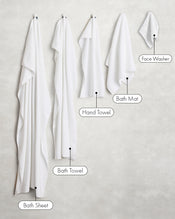 Five white linens from Bed Threads hang left to right—bath sheet, bath towel, hand towel, bath mat, and Crisp White 100% Cotton Terry Face Washers (set of two)—arranged largest to smallest. - view