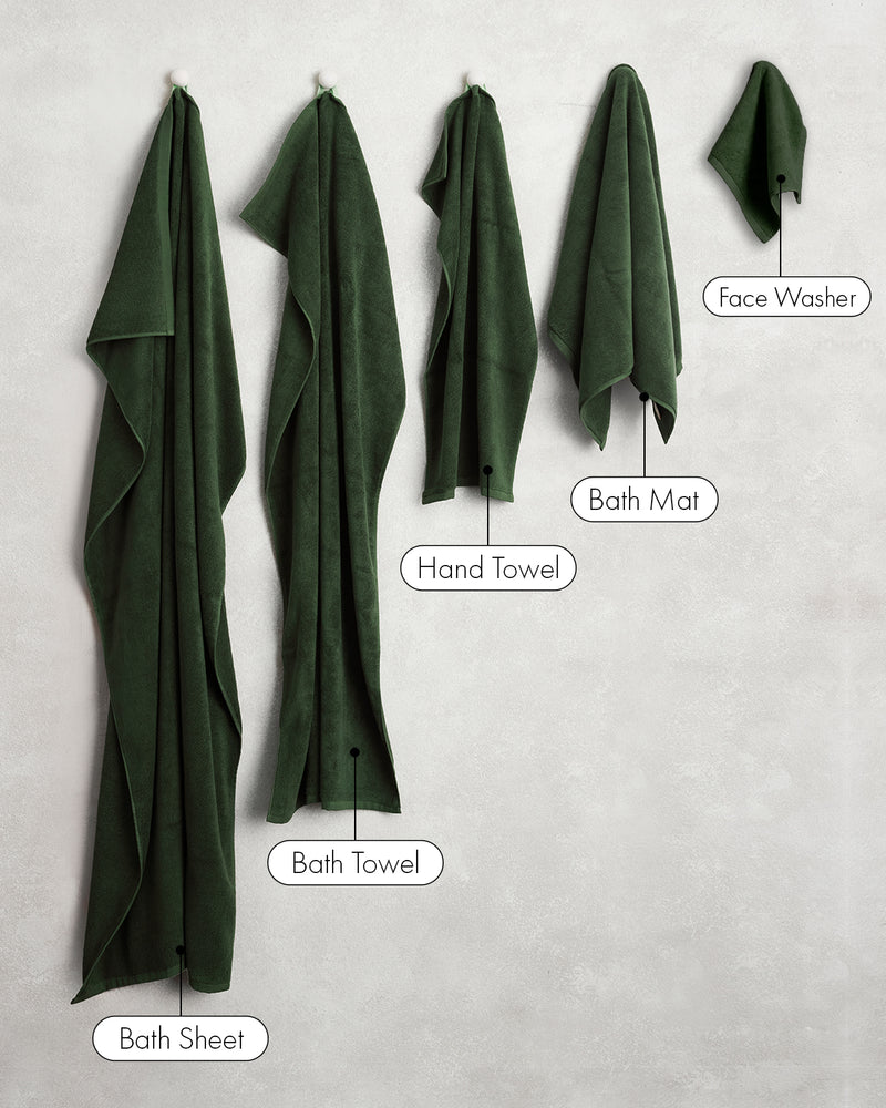 Five dark green Bed Threads Moss 100% Cotton Terry Face Washers (Set of Two) hang on hooks against a light wall, offering soft absorbency and easy care for daily use.