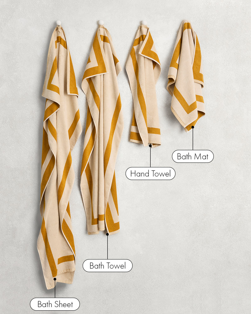 Two Crème & Turmeric Two-Toned 100% Cotton Terry Hand Towels by Bed Threads hang on the wall, showcasing their plush 650GSM fabric and quick-drying performance.