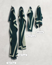 Four Forest & Sage Two-Toned 100% Cotton Terry towels by Bed Threads—Bath Sheet, Bath Towel, Hand Towel, and Bath Mat—hang against a light wall, showcasing this versatile bath towel bundle. - view