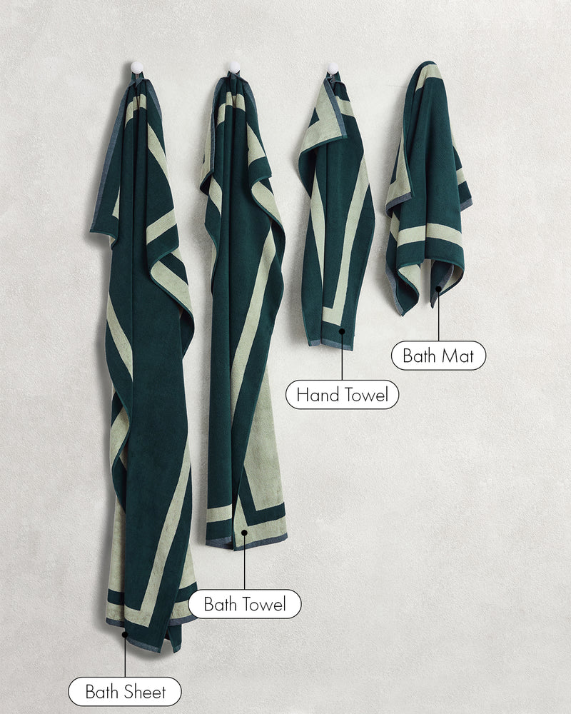 Four Forest & Sage Two-Toned 100% Cotton Terry towels by Bed Threads—Bath Sheet, Bath Towel, Hand Towel, and Bath Mat—hang against a light wall, showcasing this versatile bath towel bundle.