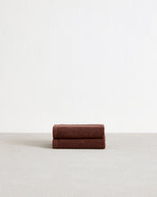 A set of two Espresso 100% Cotton Terry Face Washers by Bed Threads, soft and absorbent, rests neatly folded on a light surface with a plain white wall in the background. - view