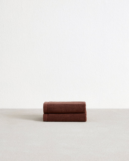 A set of two Espresso 100% Cotton Terry Face Washers by Bed Threads, soft and absorbent, rests neatly folded on a light surface with a plain white wall in the background.