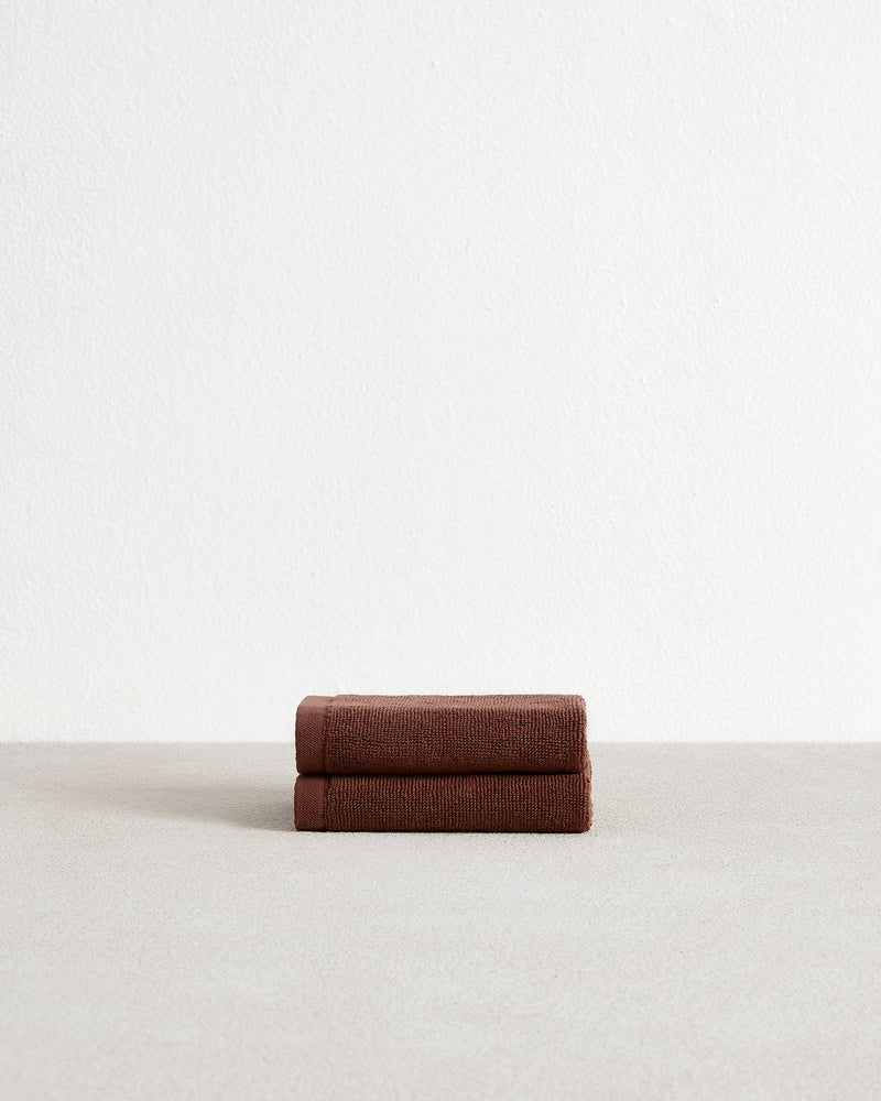 A set of two Espresso 100% Cotton Terry Face Washers by Bed Threads, soft and absorbent, rests neatly folded on a light surface with a plain white wall in the background.