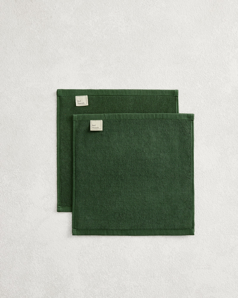 Set of two Moss 100% Cotton Terry Face Washers by Bed Threads, dark green with stitched edges and small corner labels, displayed on a light textured surface. Soft, absorbent, and ideal for daily facial care.
