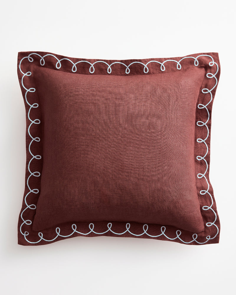 The Bed Threads Cacao & Coast 100% French Flax Linen Swirl Cushion Cover is a square maroon design with decorative white swirl edges, shown against a white background.