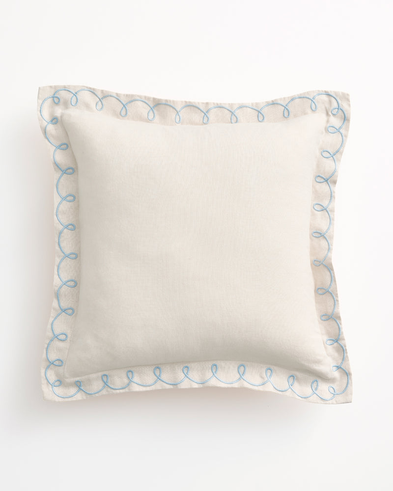 The Bed Threads Crème & Coast 100% French Flax Linen Swirl Cushion Cover features a square, off-white design with blue embroidered swirls along the edges, displayed on a plain white background.