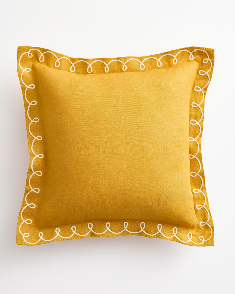 The Bed Threads Turmeric & Crème 100% French Flax Linen Swirl Cushion Cover features a square mustard yellow design with white embroidered loop and swirl edges, shown on a white background.