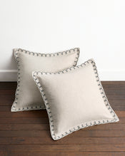A pair of Bed Threads Oatmeal & Charcoal 100% French Flax Linen Swirl European Pillowcases are styled on a wooden floor against a white wall, highlighting their elegant stitching and classic design. - view