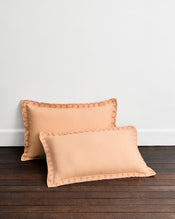 The Bed Threads Terracotta & Pink Clay 100% French Flax Linen Swirl Pillowcases (Set of Two) showcase elegant, breathable linen and swirl-embroidered edges, displayed against a dark wooden floor and a plain white wall. - view