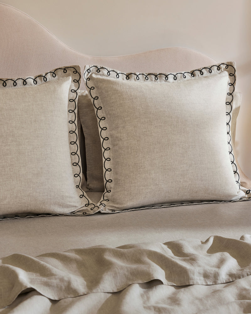 The Bed Threads Oatmeal & Charcoal 100% French Flax Linen Swirl European Pillowcases (Set of Two) add a soft, neutral touch to the bed, complementing a matching headboard and sheet for a cozy, inviting feel.