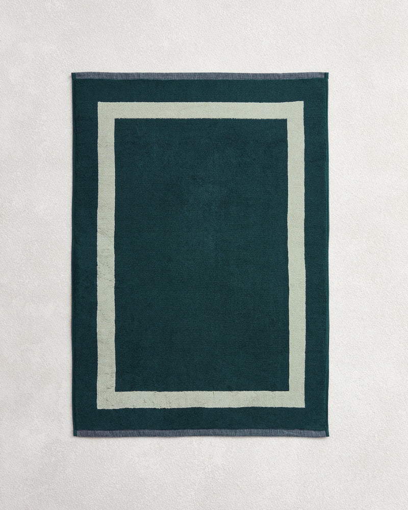 The Forest & Sage Two-Toned 100% Cotton Terry Bath Mat by Bed Threads features a rectangular dark green design with a lighter green border, shown on a light textured surface.