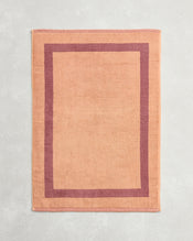 The Bed Threads Terracotta & Pink Clay Two-Toned 100% Cotton Terry Bath Mat, laid flat on a light gray textured surface, offers plush softness and a cozy feel with its warm hues. - view