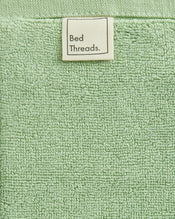 A close-up of the Apple 100% Cotton Terry Bath Mat by Bed Threads shows its light green texture and a white label at the top center, highlighting plush comfort and absorbency. - view