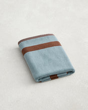 The Cacao & Lagoon Two-Toned 100% Cotton Terry Bath Mat by Bed Threads features a folded blue design with two horizontal brown stripes, shown on a light textured surface. - view