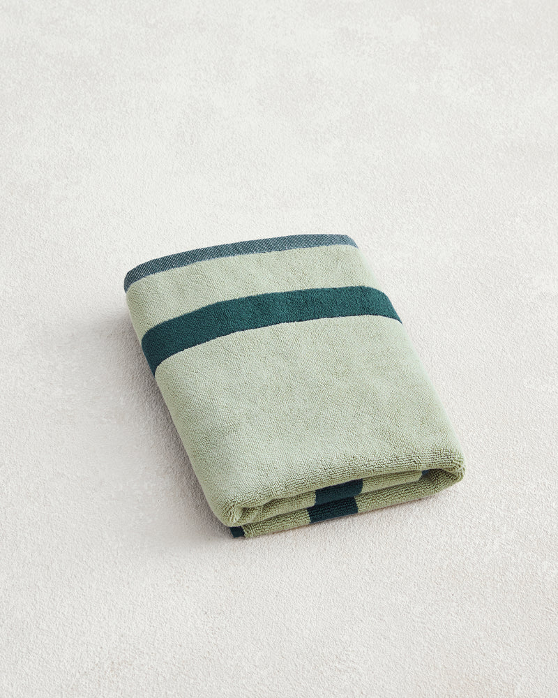 The Forest & Sage Two-Toned 100% Cotton Terry Bath Mat by Bed Threads, featuring light green with two dark green stripes, is neatly folded on a light textured surface.