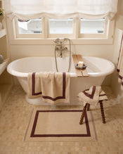 Close up of a freestanding bath tub with cotton terry towels in a creme colour with cacao border. - view