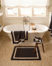 Close up of a freestanding bath tub with cotton terry towels in a charcoal colour with oatmeal border. - view
