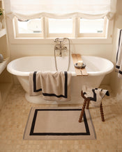 Close up of a freestanding bath tub with cotton terry towels in an oatmeal colour with charcoal border. - view