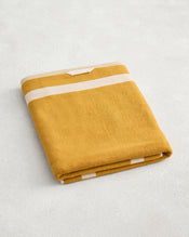 The Bed Threads Crème & Turmeric Two-Toned 100% Cotton Terry Bath Sheet, plush and quick-drying, is folded neatly on a light surface, showcasing its soft yellow and white striped design. - view