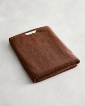 The Bed Threads Espresso 100% Cotton Terry Bath Sheet, neatly folded with a small white tag, rests on a light gray surface. - view