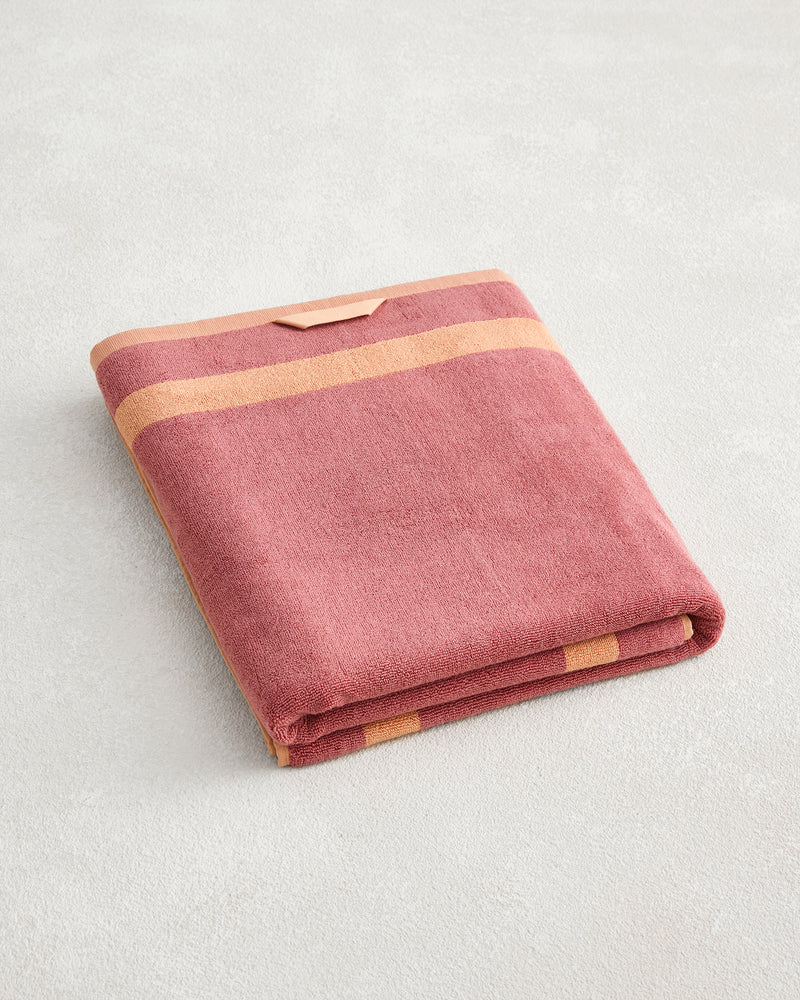 The Bed Threads Terracotta & Pink Clay Two-Toned 100% Cotton Terry Bath Sheet, crafted for a touch of luxury and quick drying, features soft pink and terracotta shades and rests on a textured surface.