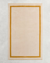 The Bed Threads Crème & Turmeric Two-Toned 100% Cotton Terry Bath Sheet adds cozy style to your bathroom, especially when paired with a rectangular beige rug on a light grey textured surface for an inviting touch. - view