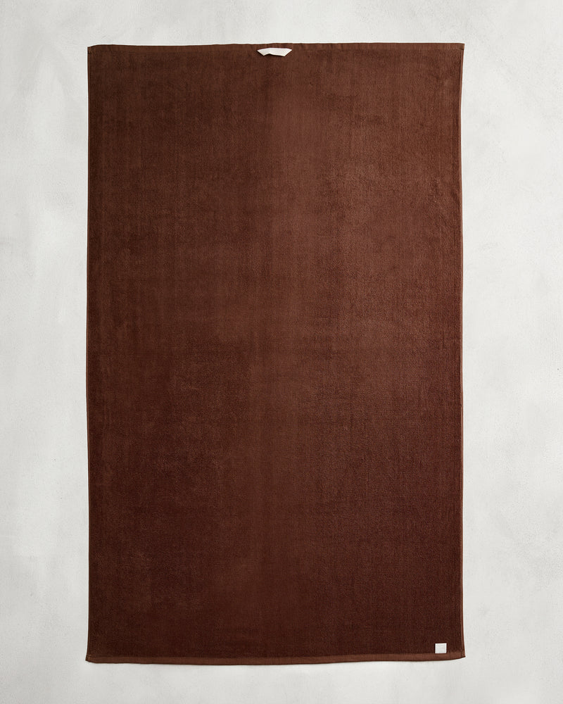 The Bed Threads Espresso 100% Cotton Terry Bath Sheet, large and rectangular with a plush texture, is laid flat on a light gray surface, showing a small white tag in one corner and a hanging loop at the top.