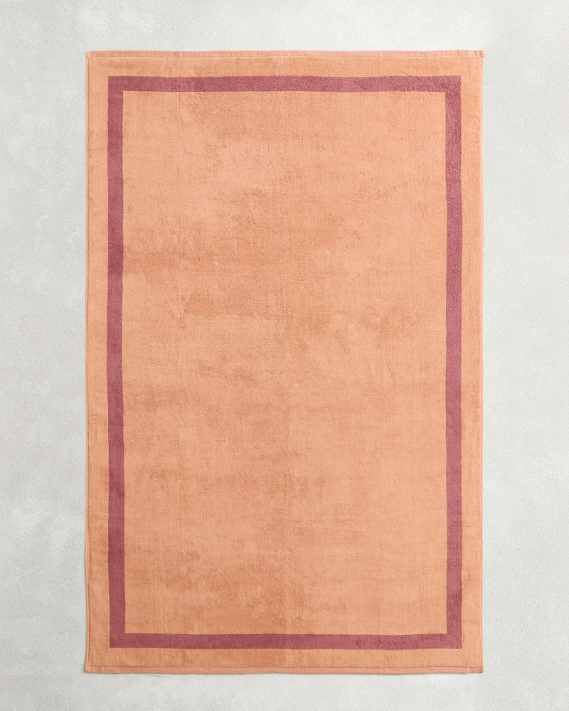 A set of Bed Threads Terracotta & Pink Clay Two-Toned 100% Cotton Terry Bath Sheets, featuring a contrasting border, is displayed flat on a light gray textured background.