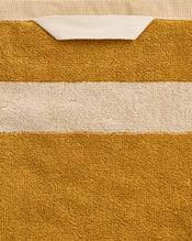 A close-up of the Bed Threads Crème & Turmeric Two-Toned 100% Cotton Terry Bath Sheet, featuring a mustard yellow quick-drying towel with a white stripe and folded edge; plush texture and stitching are clearly visible. - view