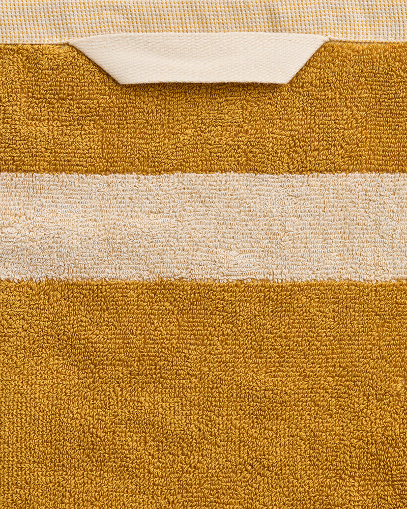 A close-up of the Bed Threads Crème & Turmeric Two-Toned 100% Cotton Terry Bath Sheet, featuring a mustard yellow quick-drying towel with a white stripe and folded edge; plush texture and stitching are clearly visible.